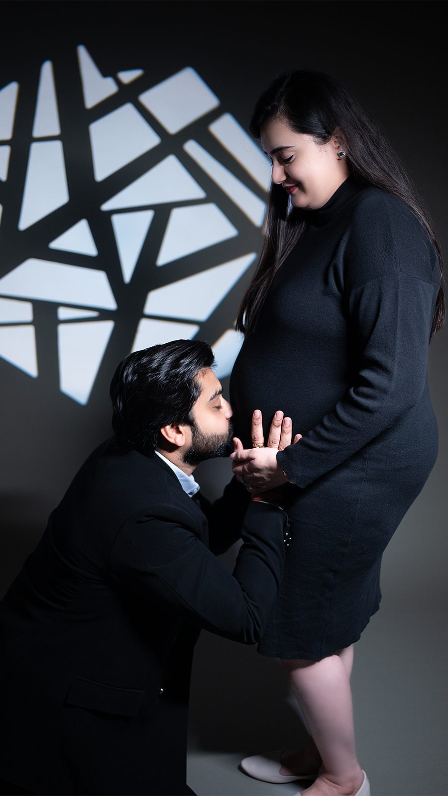 Father kissing baby bump with geometric studio backdrop maternity shoot