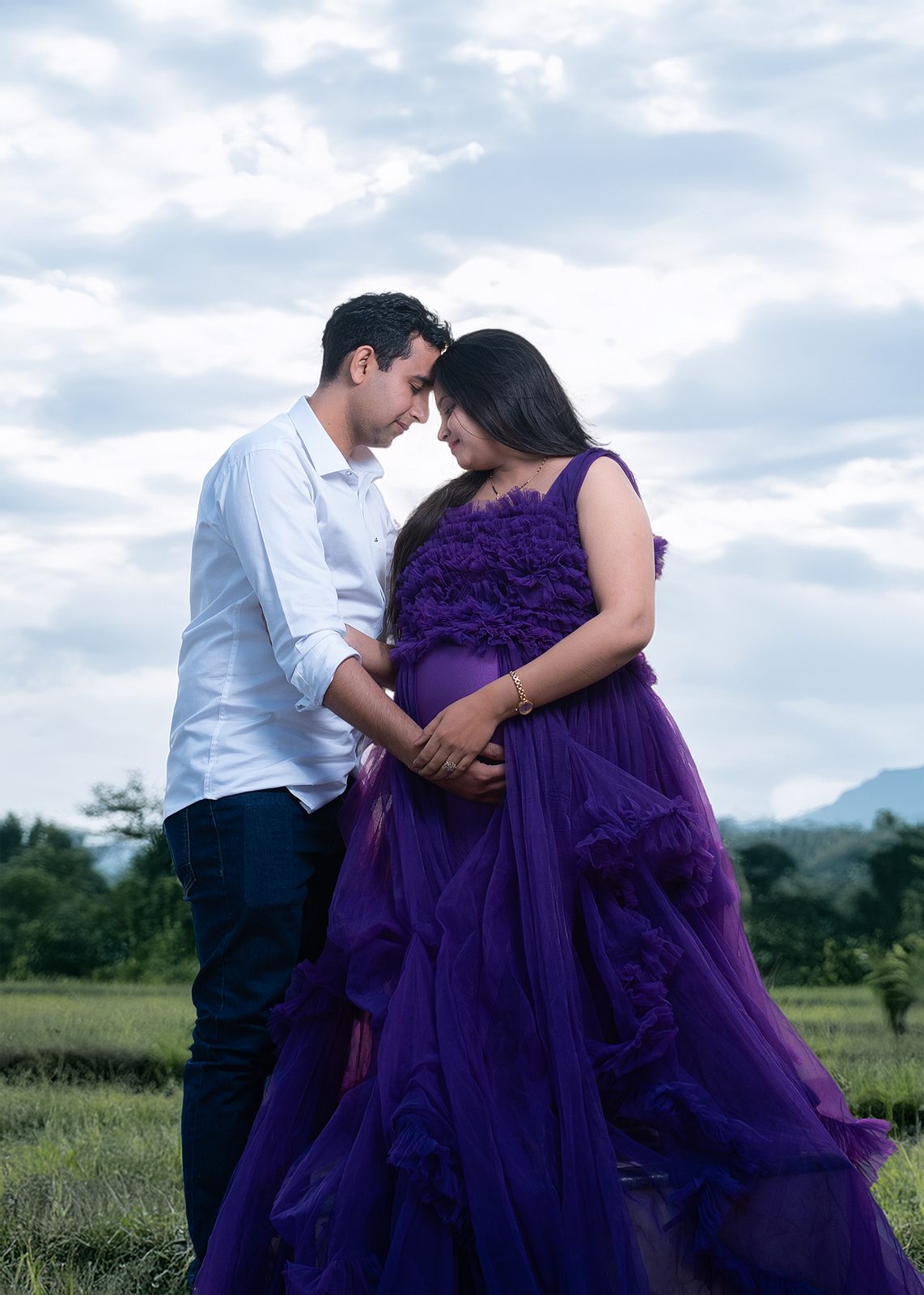 Outdoor maternity couple shoot in purple gown with cloudy sky landscape